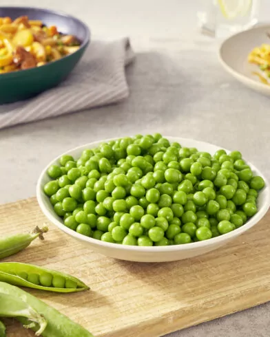 Egy tál FRoSTA fagyasztott borsó és tészta áll a vágódeszkán.